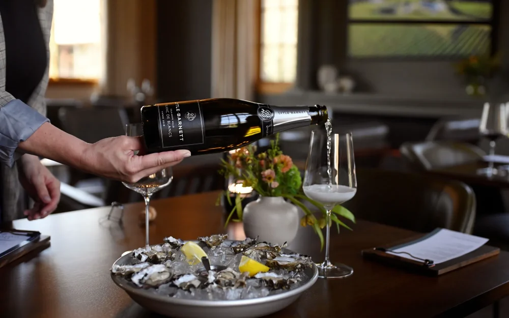 Hand pouring a glass of Lytle Barnett Blanc de Blancs sparkling wine served with oysters