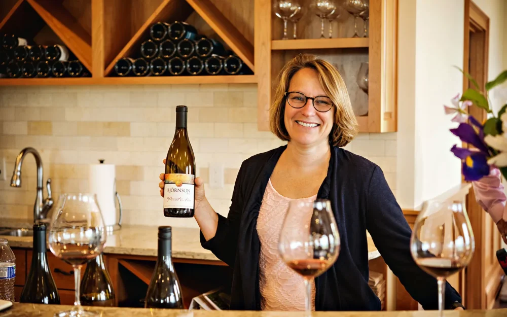 Pattie Bjornson, owner of Bjornson Vineyard, holding a bottle of wine in the tasting room