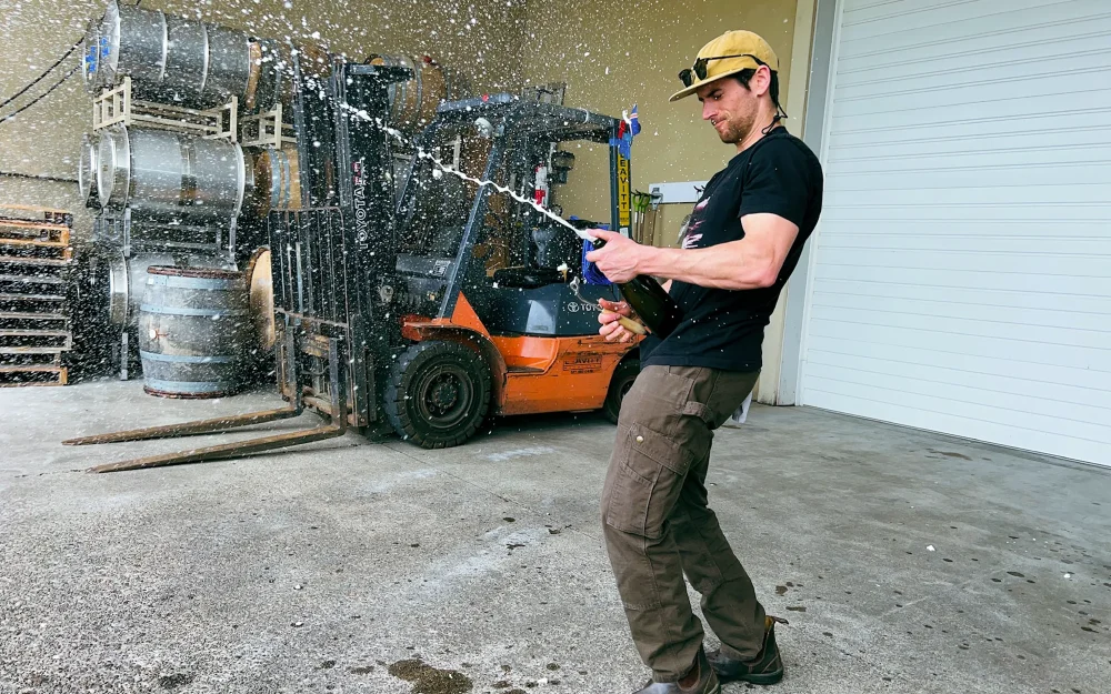 Kenny McMahon spraying a bottle of sparkling wine