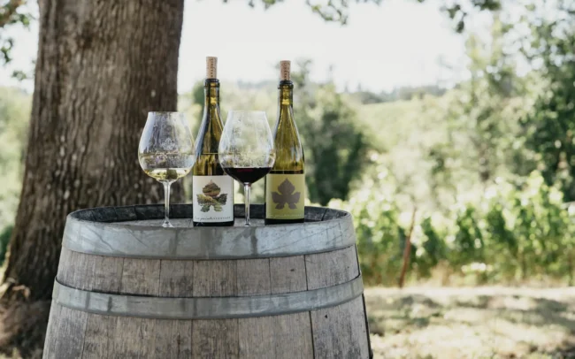 Bottles and glassware of Five Points wine on top of a wine barrel